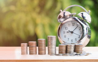 Stacks of coins in ascending order next to a silver retro alarm clock