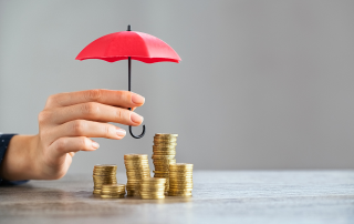 a hand holding a red umbrella over stacks of gold coins, representing protecting your retirement savings