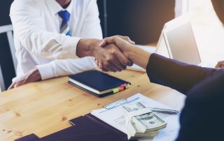 two people shaking hands with money on the table